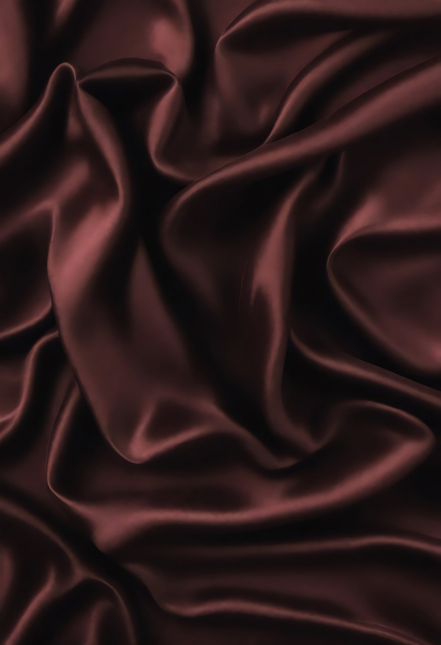 Rich burgundy satin fabric draped elegantly on a surface, showcasing deep folds and a luxurious sheen in soft lighting