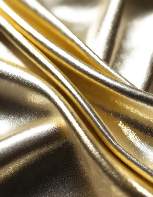 Metallic golden and silver fabric creates elegant textures with intricate folds and reflections under soft lighting
