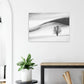 Poster of a lone bare tree among black and white snowy hills above a wooden console beside a plant