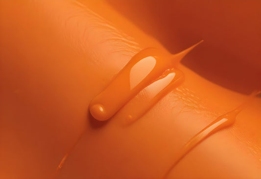 Close-up of glossy orange liquid dripping on smooth surface in a warm, illuminated setting. Generative AI