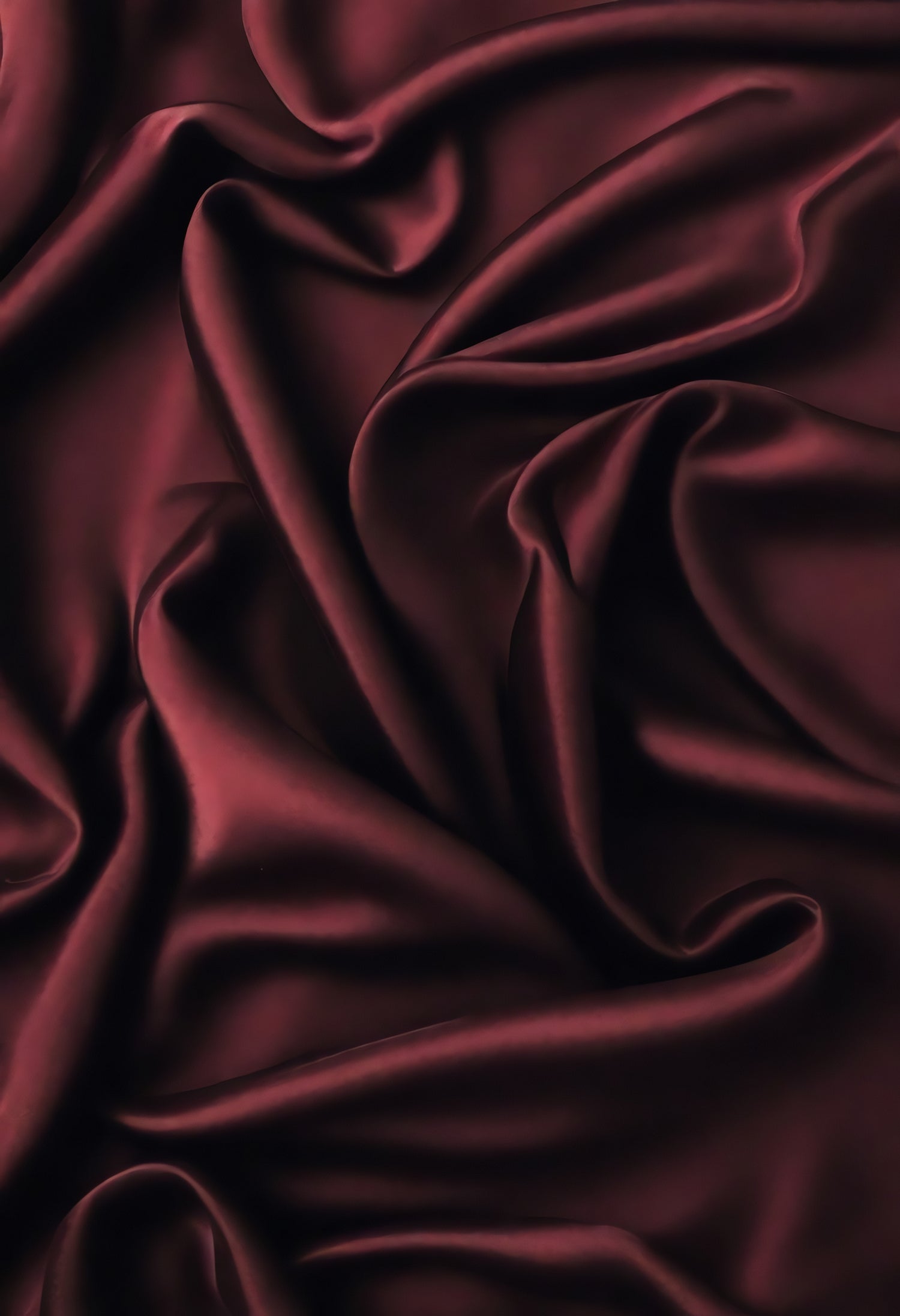 Rich burgundy satin fabric drapes elegantly, showcasing delicate folds and textures in soft light during afternoon