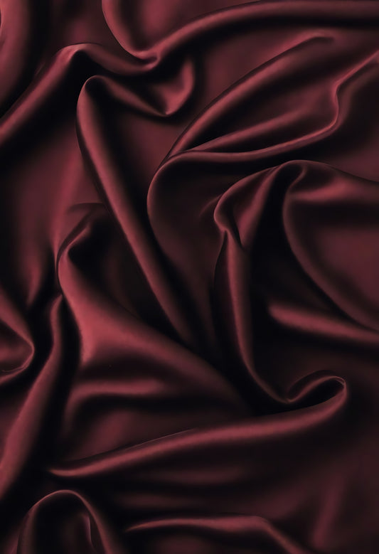 Rich burgundy satin fabric drapes elegantly, showcasing delicate folds and textures in soft light during afternoon