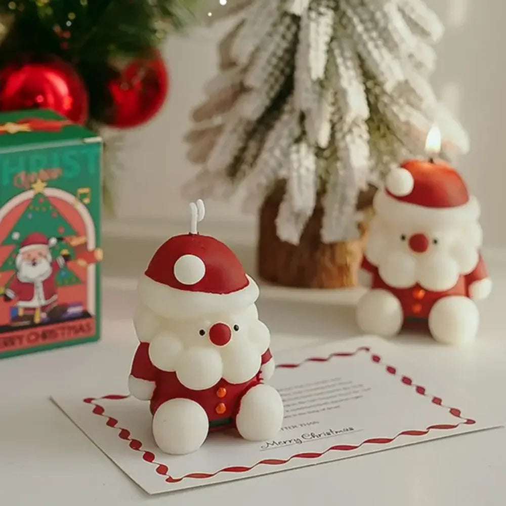 Two Santa Claus-shaped candles on a Christmas card with a decorated tree in the background.