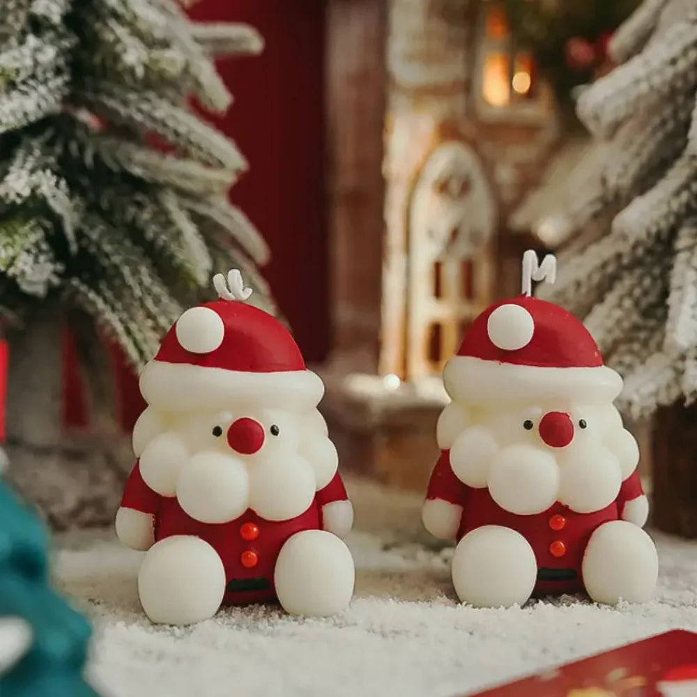 Two Santa Claus figurines on a snowy surface with Christmas decorations in the background.