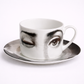 Ceramic cup and saucer with artistic face design on a white background