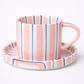 Ceramic mug and saucer with pink and blue striped design on a white background