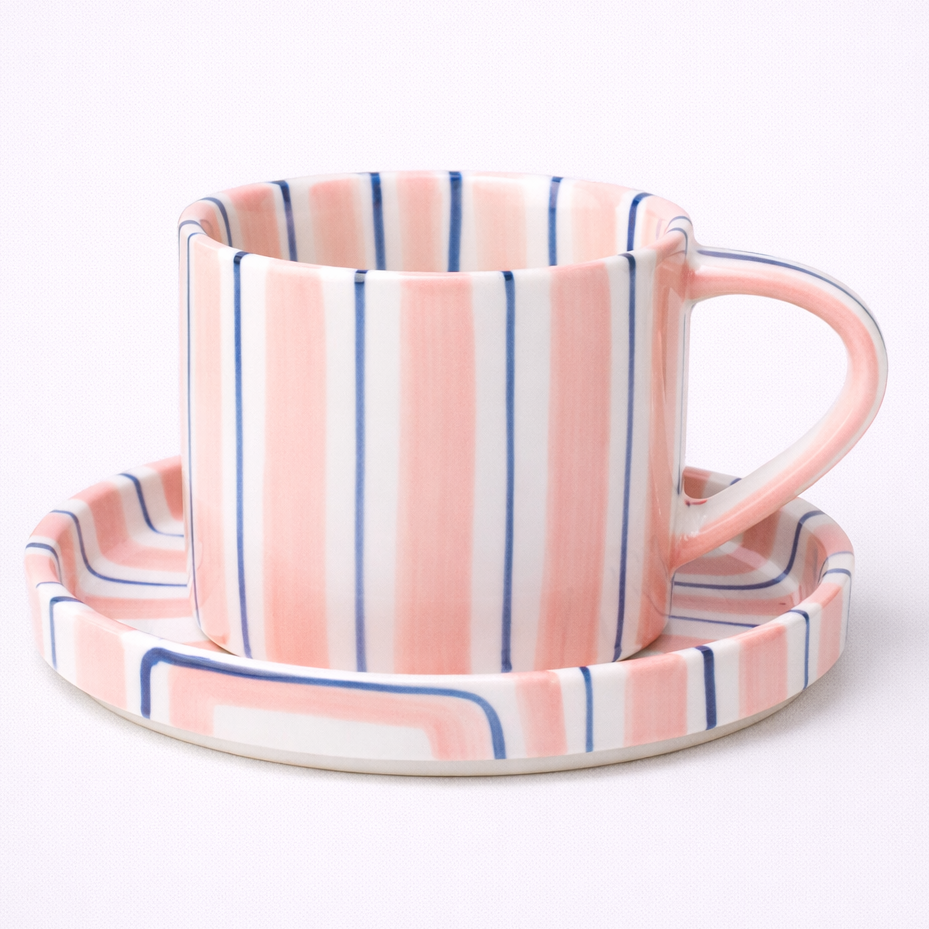 Ceramic mug and saucer with pink and blue striped design on a white background