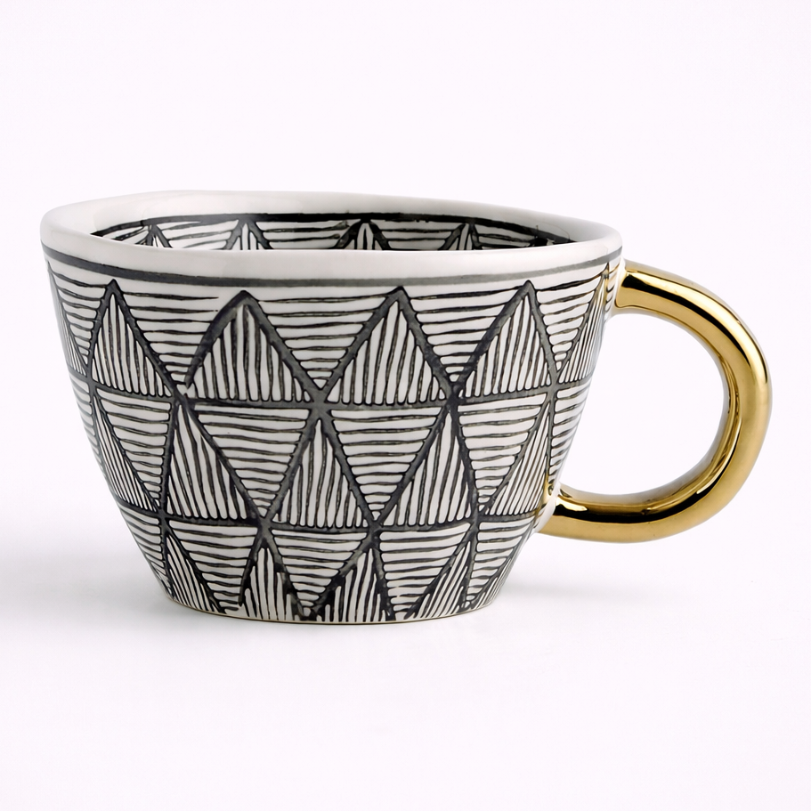 Ceramic mug with geometric black pattern and gold handle on a white background
