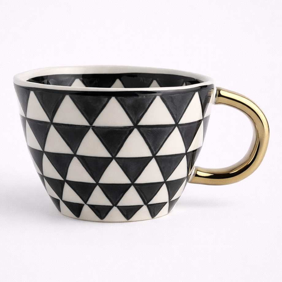 Mug with black and white triangle pattern and gold handle on a white background