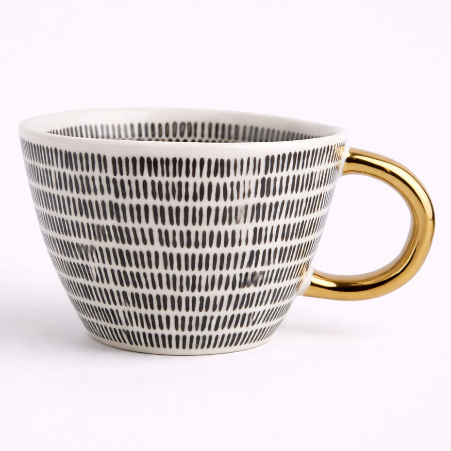 White mug with black pattern and gold handle on a white background