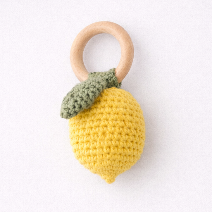 Crocheted lemon-shaped teething ring with a wooden ring on a white background