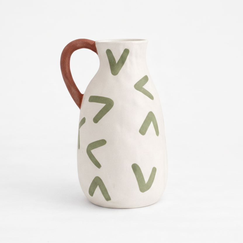 Ceramic pitcher with green leaf patterns on a white background