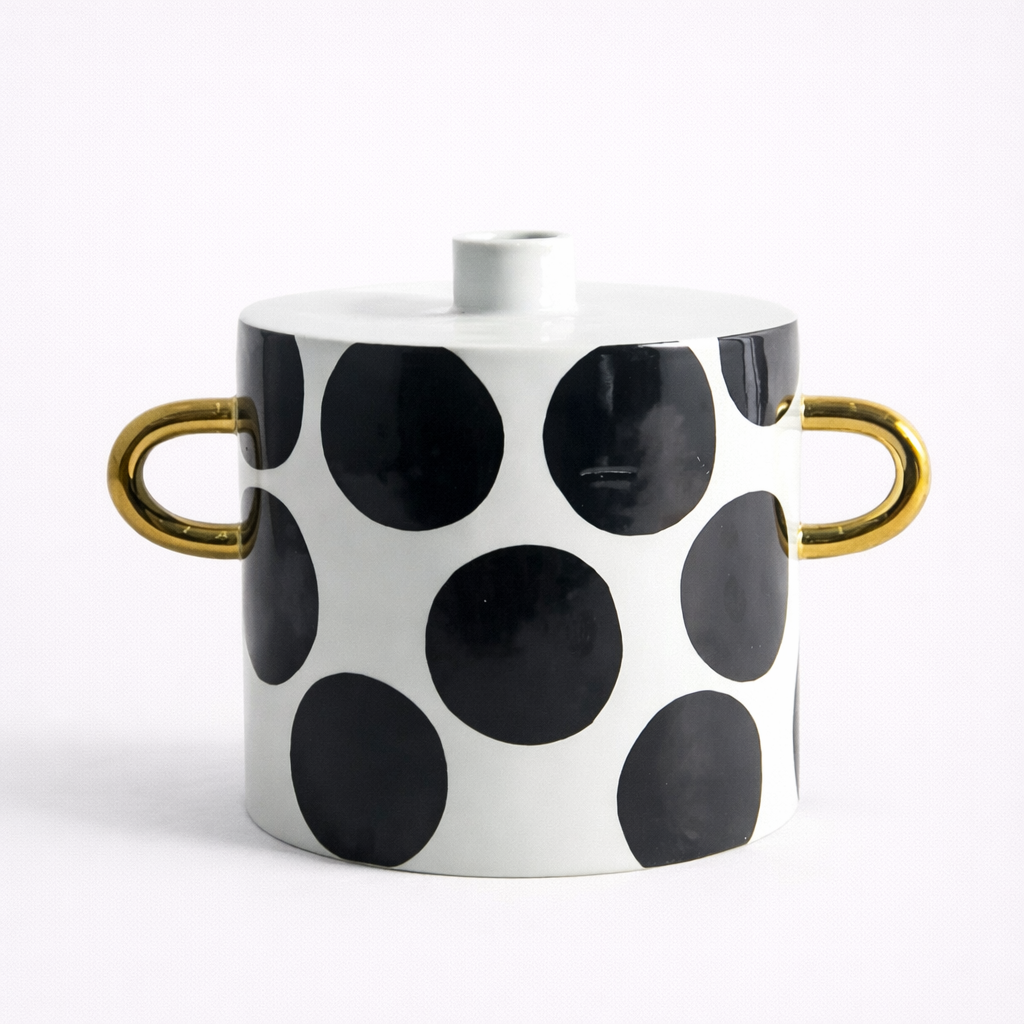 Ceramic pot with black polka dots and gold handles on a white background.