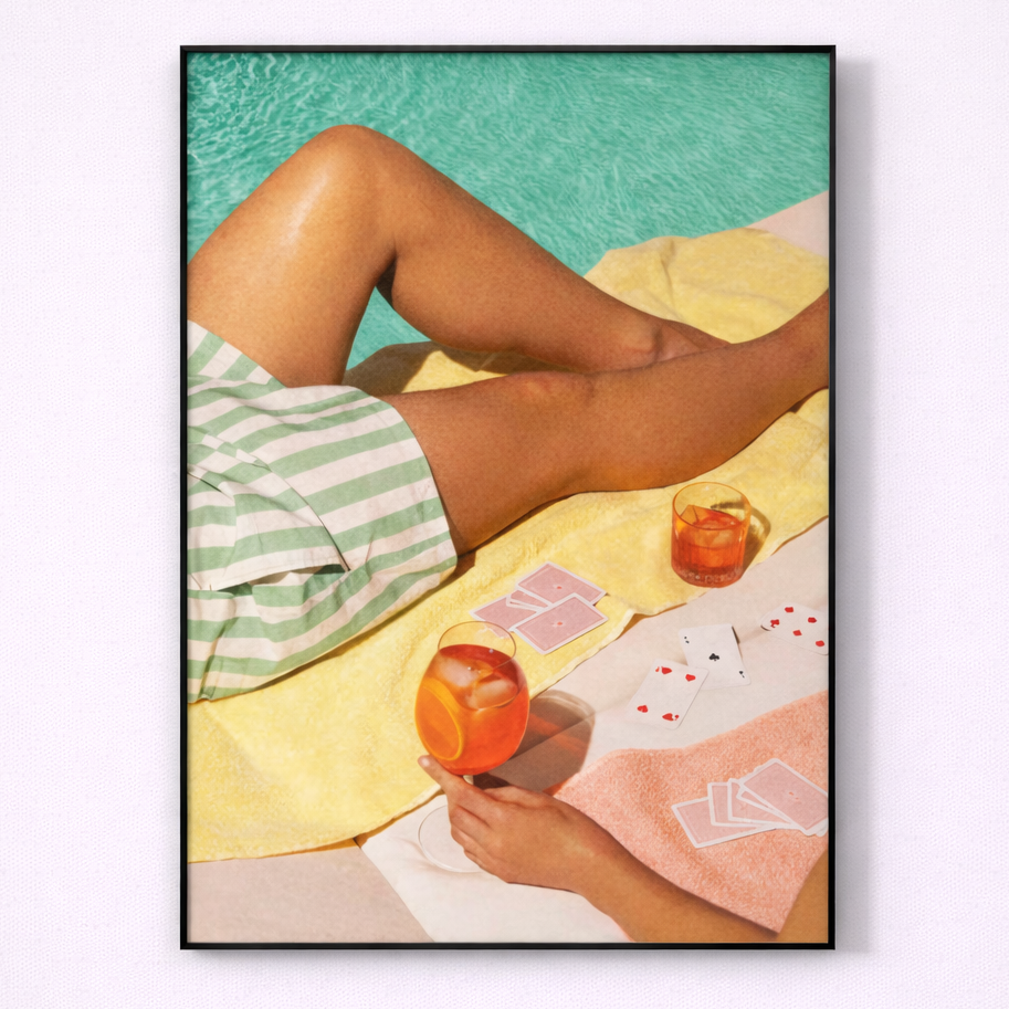 Framed artwork of a person lounging by a pool with an orange and playing cards.