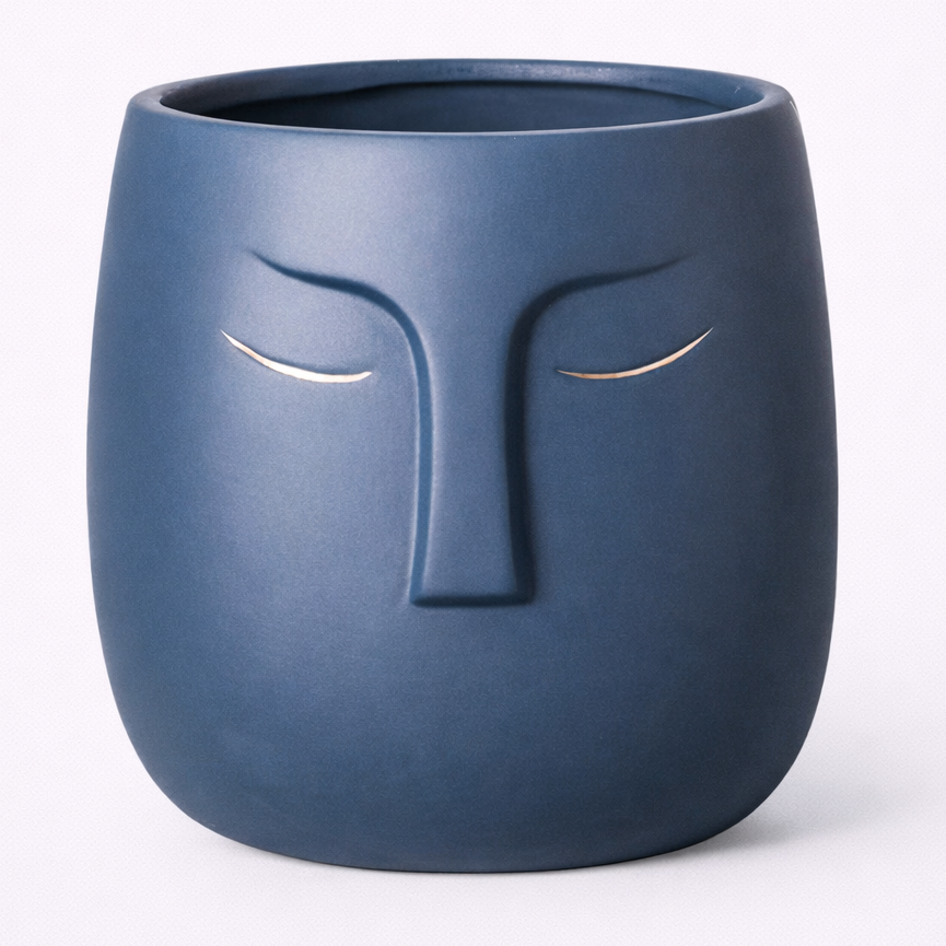 Blue ceramic pot designed like a face with closed eyes on a white background