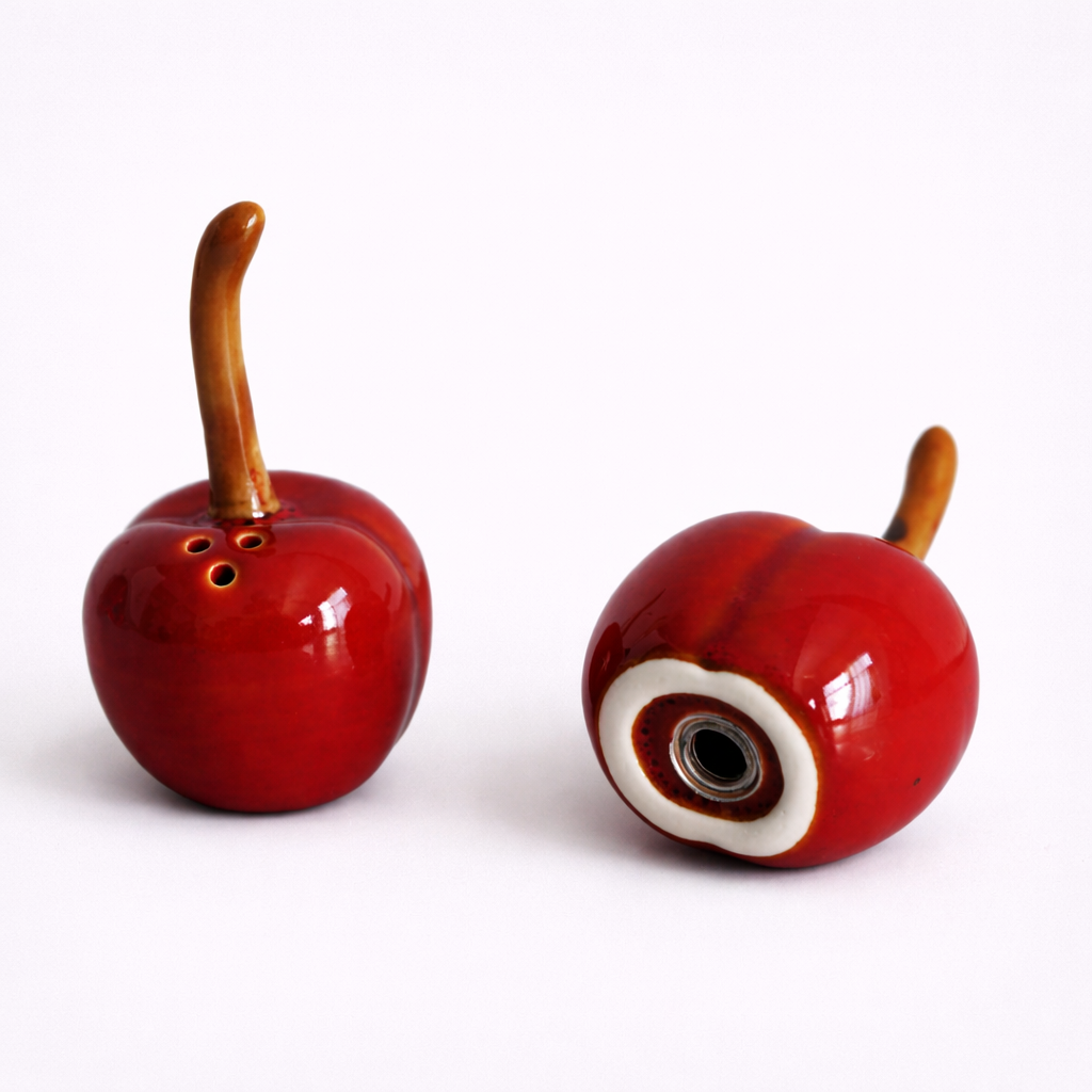Two red ceramic cherries with wooden stems on a white background
