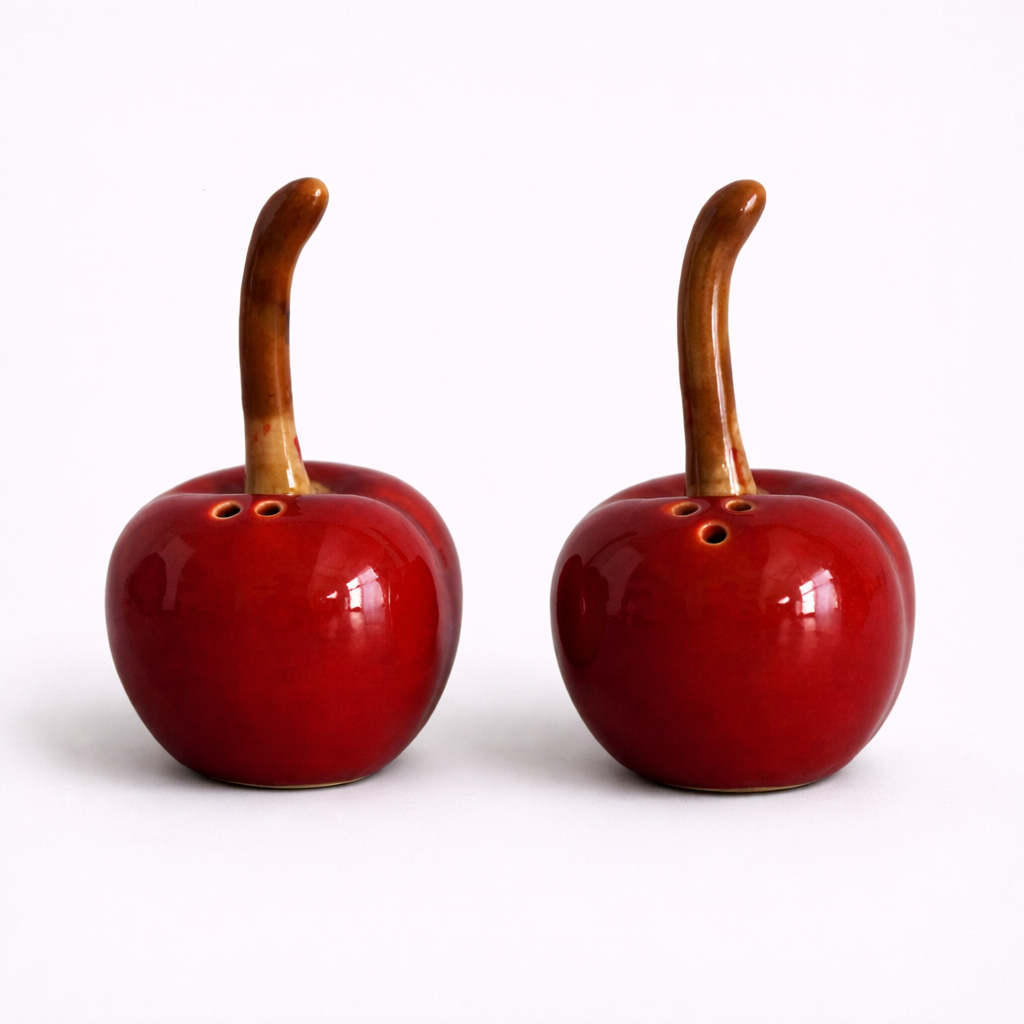 Two red ceramic apple-shaped salt and pepper shakers with wooden stems on a white background.