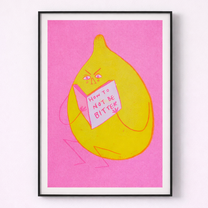 Framed artwork of a lemon character holding a book titled 'How to Not Be Bitter' on a pink background
