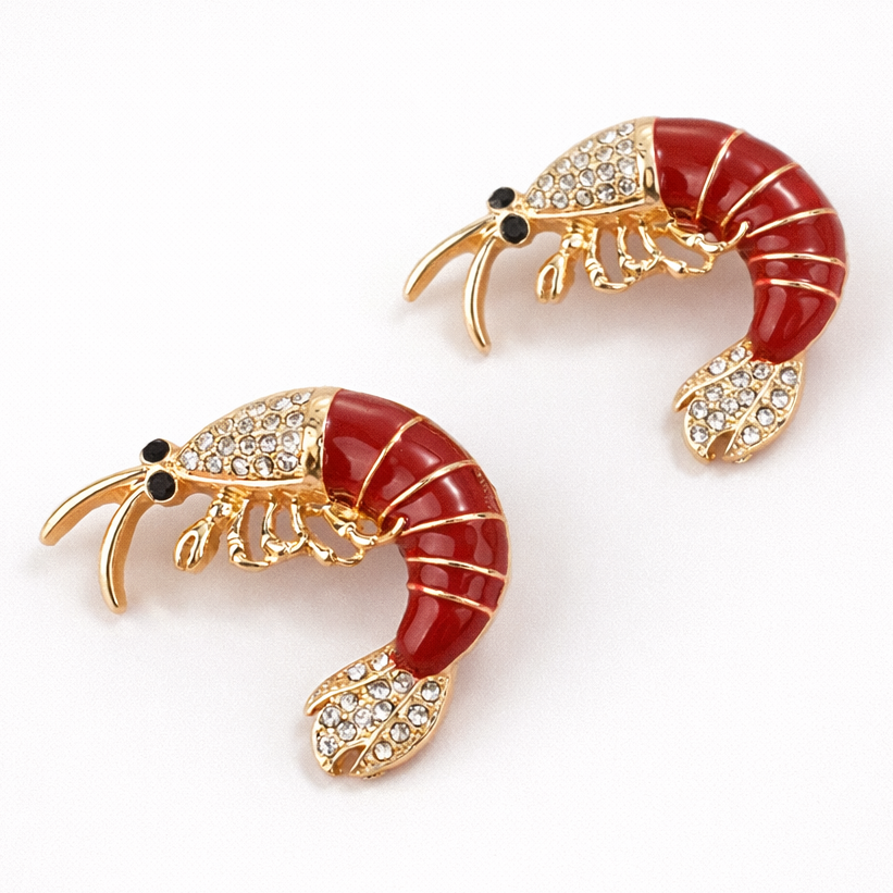 Pair of shrimp-shaped earrings with red bodies and gold accents on a white background