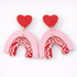 Pair of earrings with pink arches and red hearts on a white background