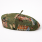 Green beret with embroidered scenes on a white background
