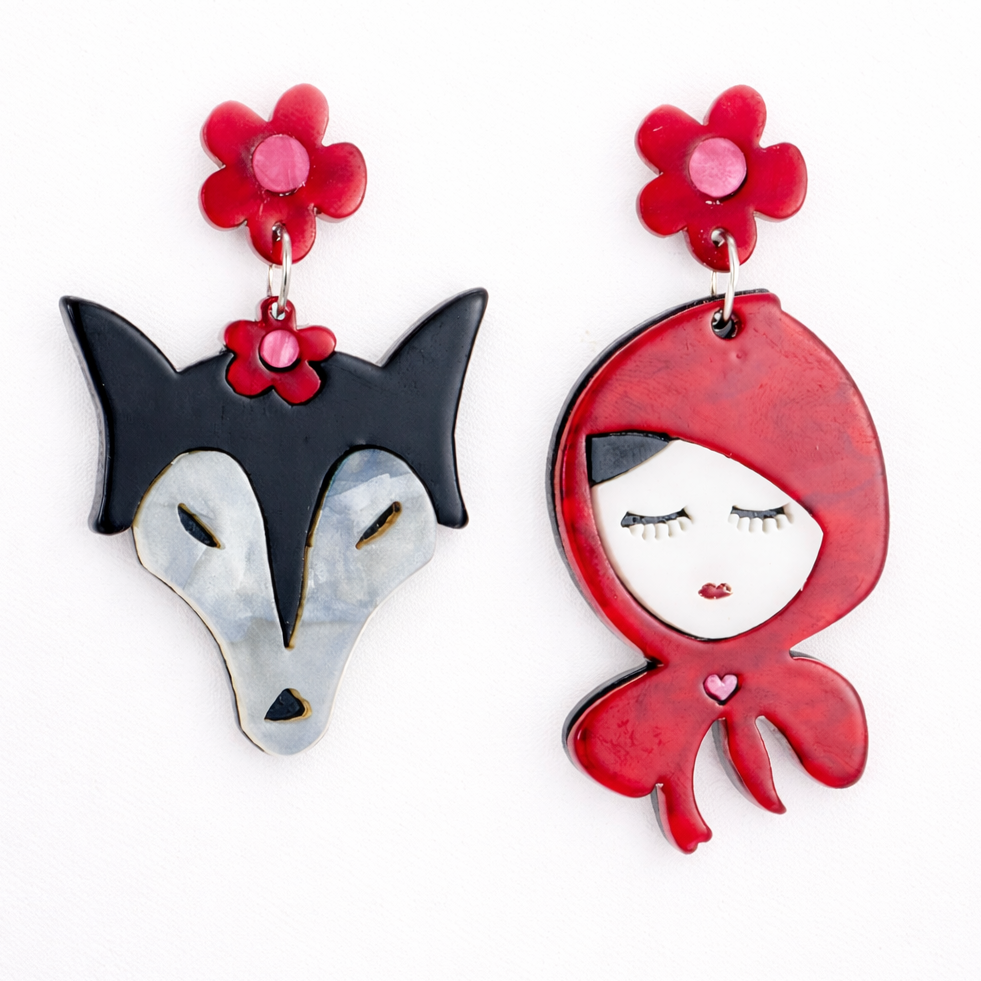 Pair of earrings featuring a wolf and a hooded figure with flower details on a white background