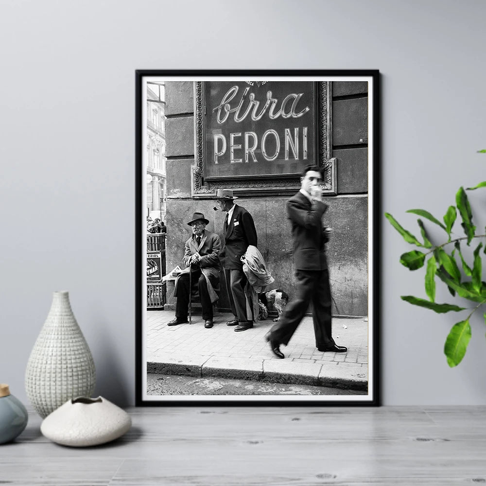 Framed black and white photo of people on a street with 'Birra Peroni' sign, placed on a wooden floor.