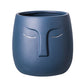 A blue ceramic vase with a geometric pattern resembling a face on the front.