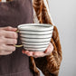 Person holding a striped ceramic mug with a neutral background