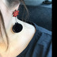 Close-up of a person wearing a unique earring with a red flower and black circular design.