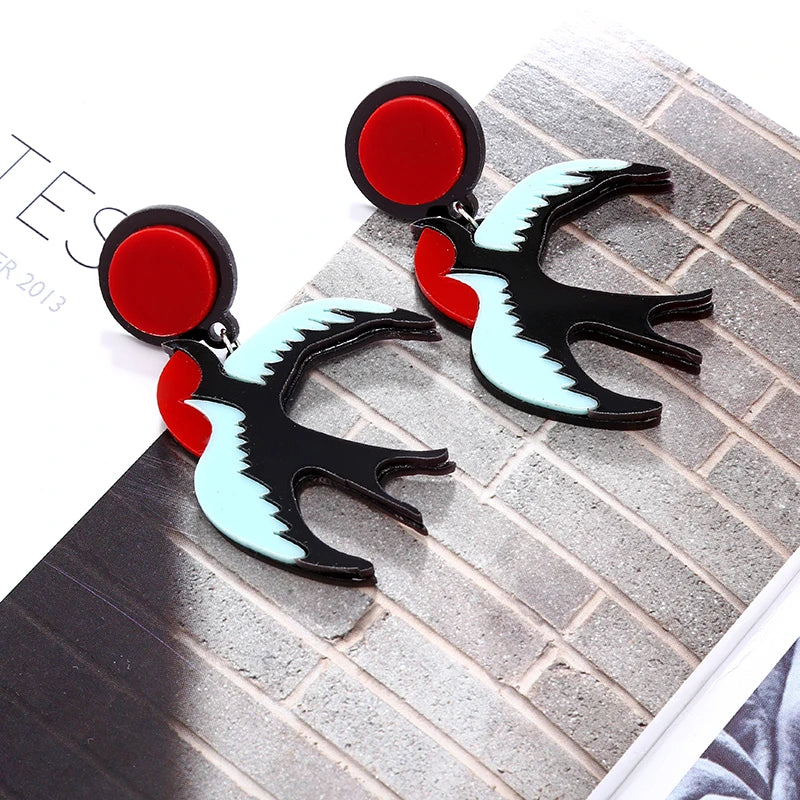 Pair of earrings with red, black, and light blue design on a textured surface