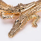Gold crocodile-shaped brooch with gemstones on a white background