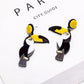 Toucan-shaped earrings on a white surface with 'PAR City Guide' text in the background.