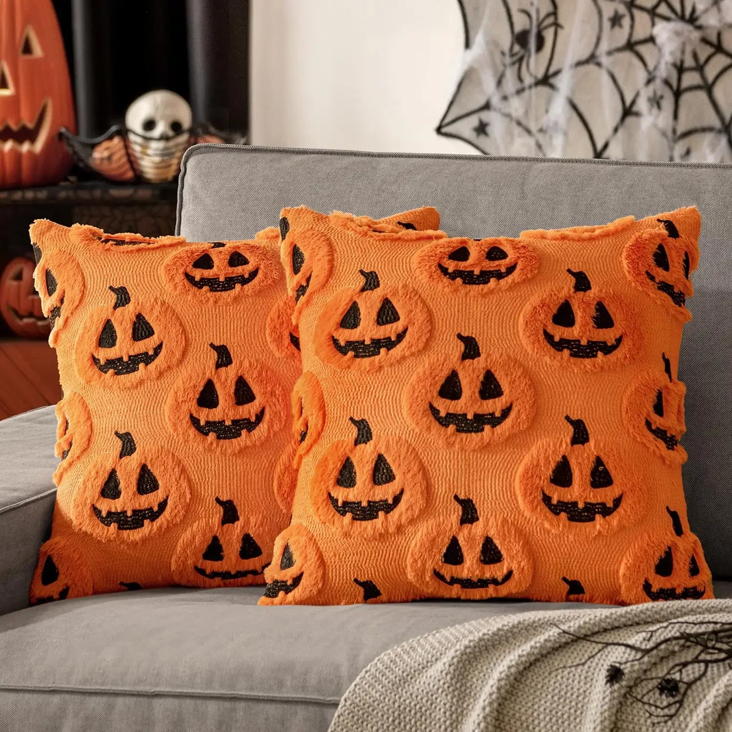 Orange pillows with black jack-o'-lantern faces on a gray couch, Halloween-themed decor.