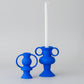 Blue candle holders with white candles on a book in a room with a window.