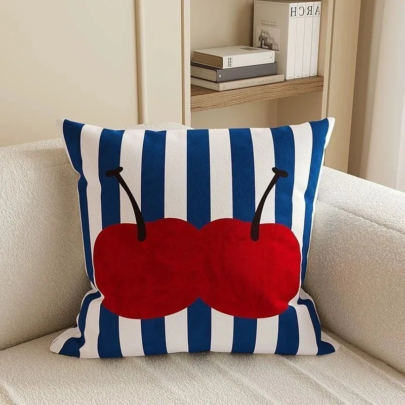 Decorative pillow with red cherries and blue and white stripes on a beige couch.
