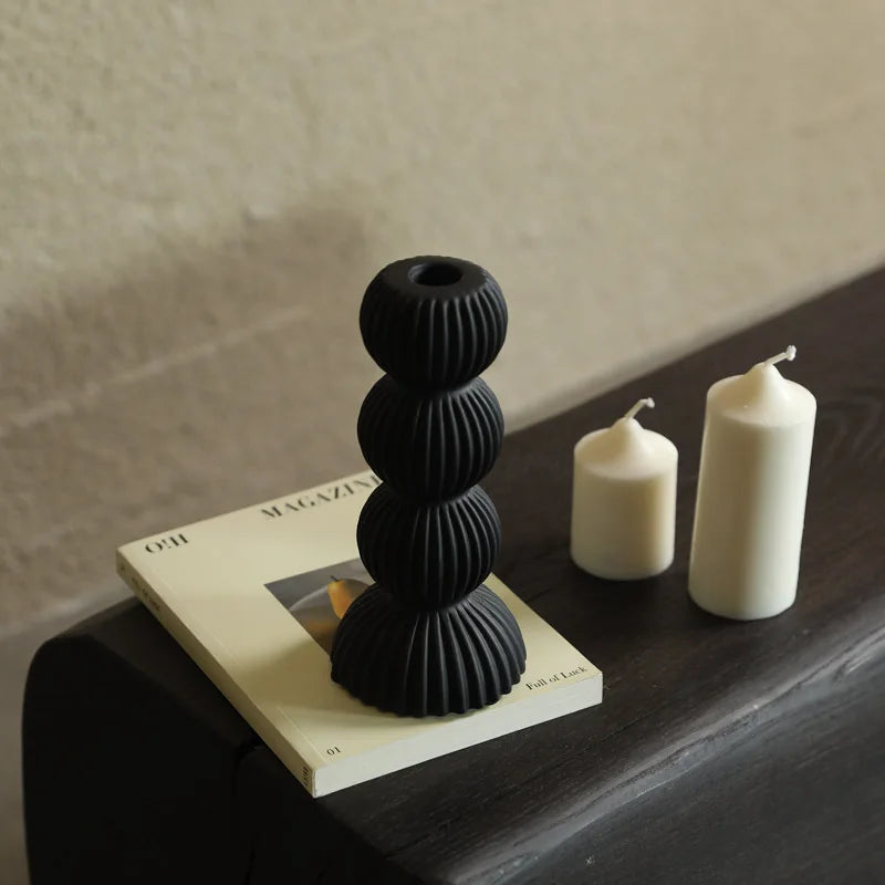 Black textured candle holder on a magazine with two white candles on a wooden surface.