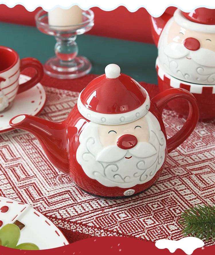 Red teapot shaped like a Santa Claus face on a table with Christmas decor.