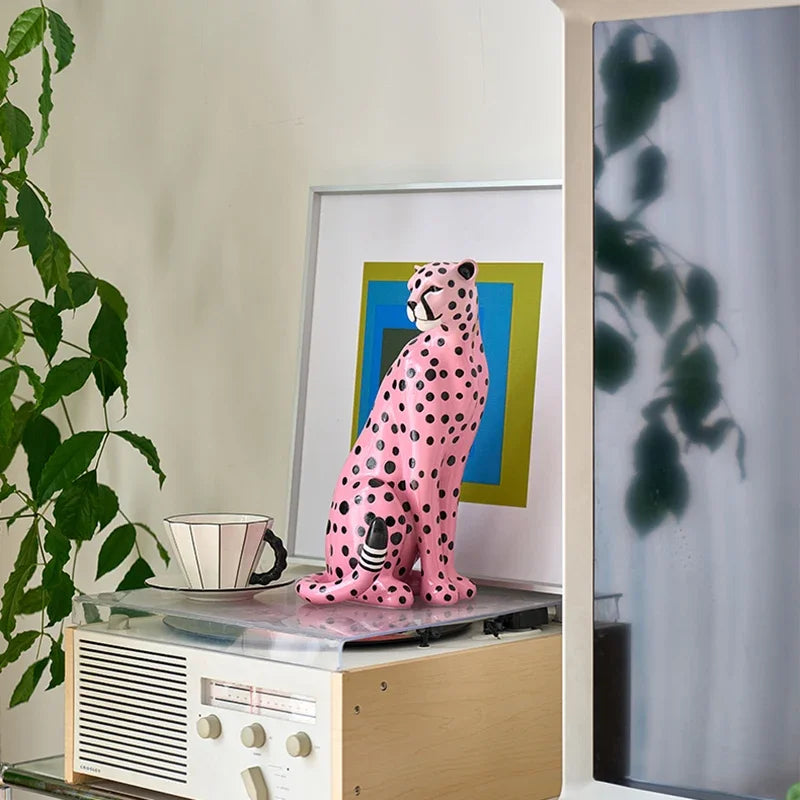 Pink and black polka dot cat figurine on a vintage radio with a plant and framed picture in the background.