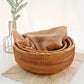 Woven basket with a beige towel on a light surface with a blurred plant in the background