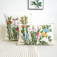 Two floral-patterned pillows on a bed with a white wall and framed artwork in the background.