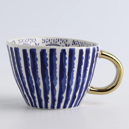 Ceramic mug with blue striped design and gold handle on a light gray background