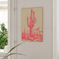 Framed artwork of a red cactus on a beige background in a room with a window and plant.