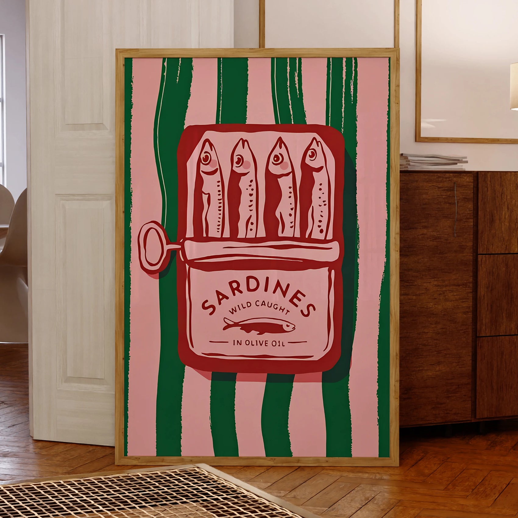 Framed artwork of a sardine can design on a pink and green striped background in a room.