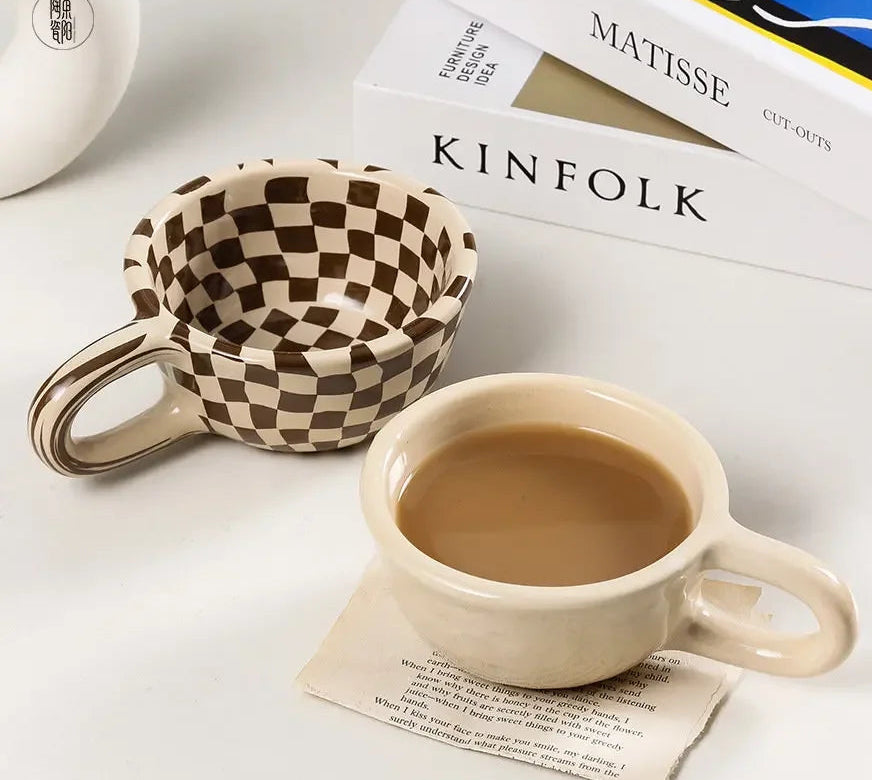 Checkered mug, coffee cup, and 'KINFOLK' magazine on a white surface with 'zizi fish' branding.