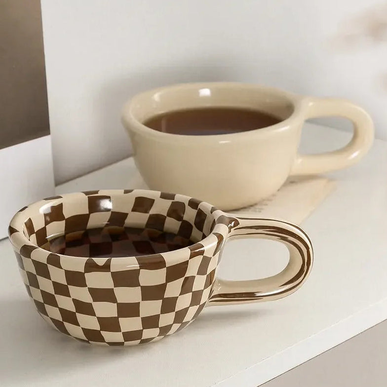 Checkered ceramic mug and beige cup on a surface with 'zizi fish' branding.