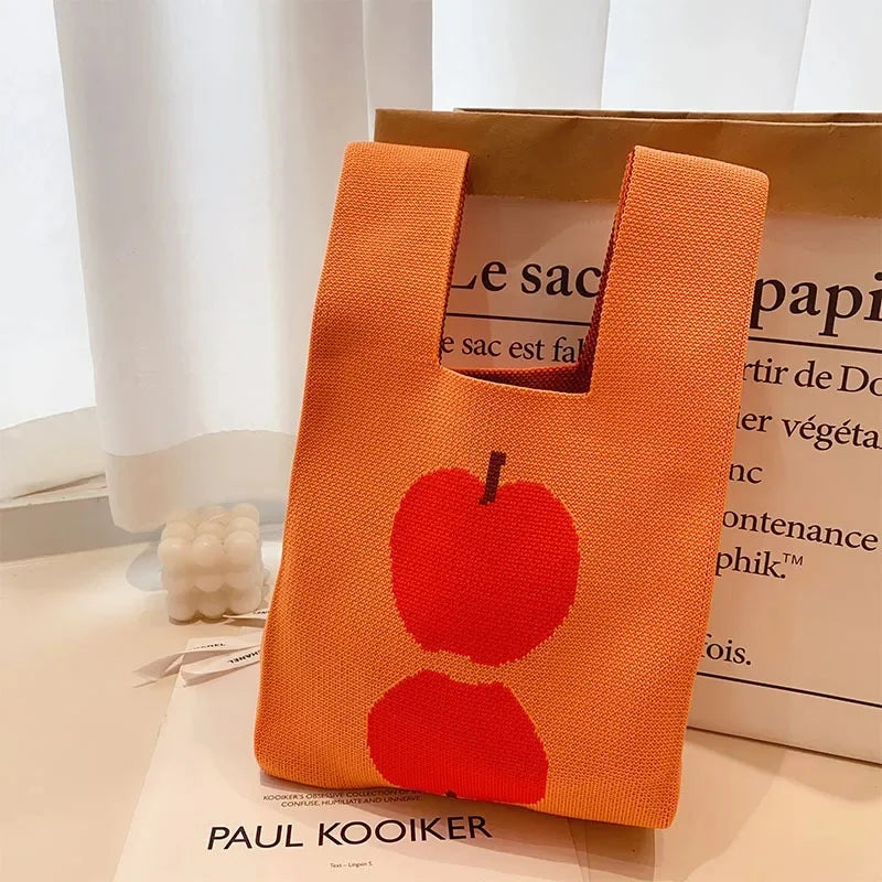 Orange tote bag with red apple design on a white surface, branded 'Paul Kooiker'.