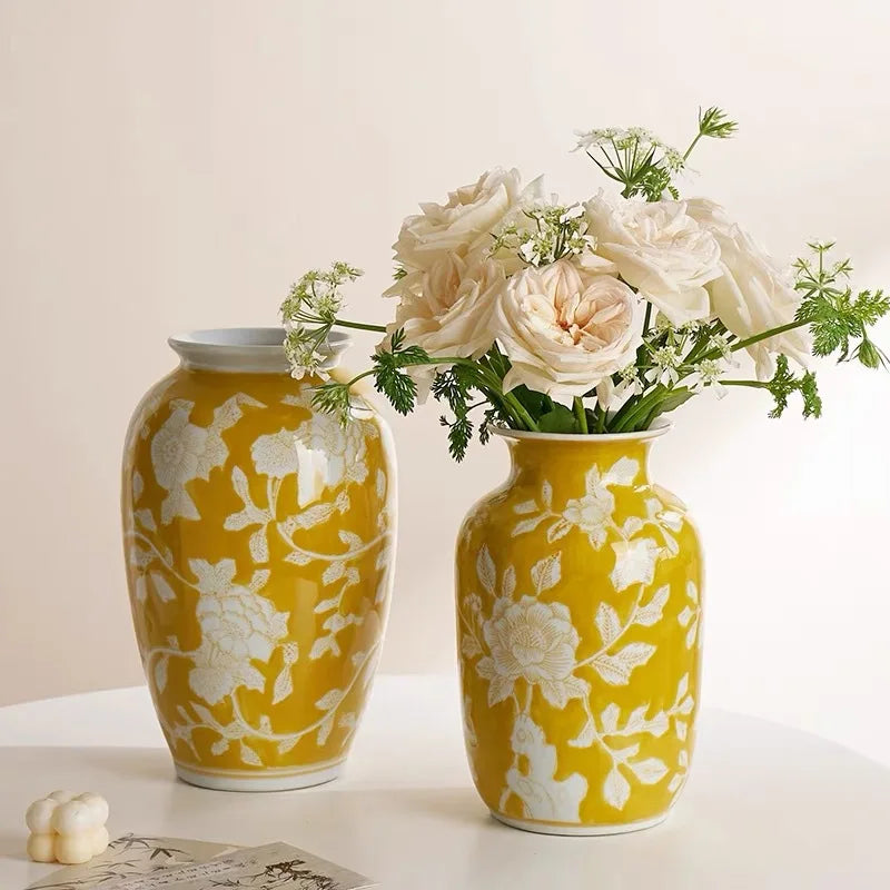 Two yellow vases with white floral patterns, one holding flowers on a light background.