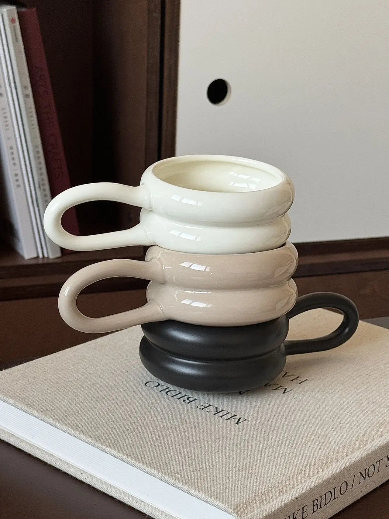 Stacked ceramic mugs in white, beige, and black on a book