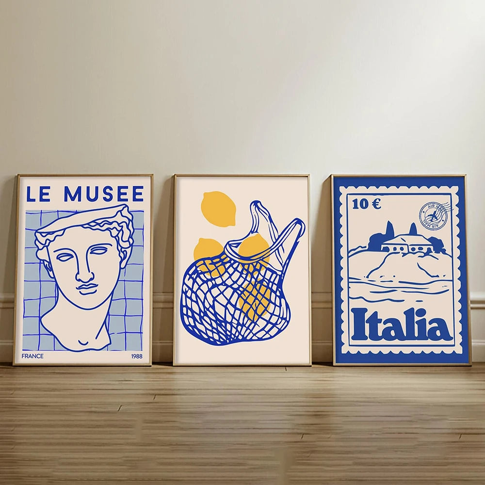 Three framed artworks on a wooden shelf against a beige wall.